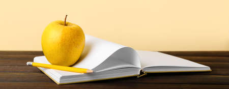 School notebook with apple and pencil on table against yellow backgroundの写真素材