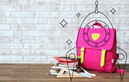 Drawn rocket with school backpack and stationery on table against brick background with space for...