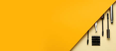 Black mascara, tweezers and fake eyelashes on yellow background with space for textの写真素材