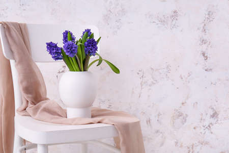 Vase with beautiful flowers on chair near light wallの写真素材