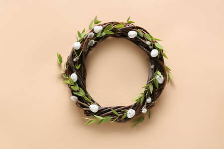 Beautiful wreath with Easter eggs and green branches on beige backgroundの写真素材