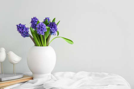 Vase with beautiful flowers, books and decor on table near light wallの写真素材