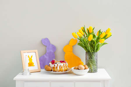 Easter cake, eggs, tulips, burning candle and decor on table near light wallの写真素材