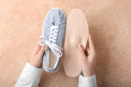 Female hands with beige orthopedic insole and shoe on beige backgroundの写真素材
