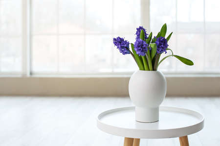 Vase with beautiful flowers on table in light roomの写真素材
