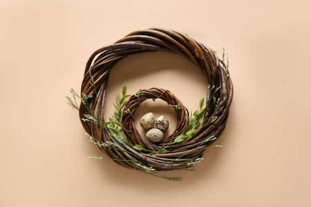 Beautiful wreath with Easter eggs and green branches on beige background