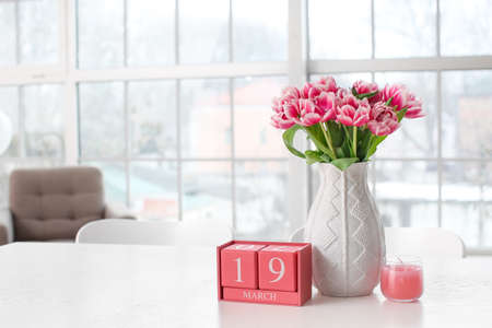 Vase with beautiful tulips, cube calendar and candle on table in light roomの写真素材