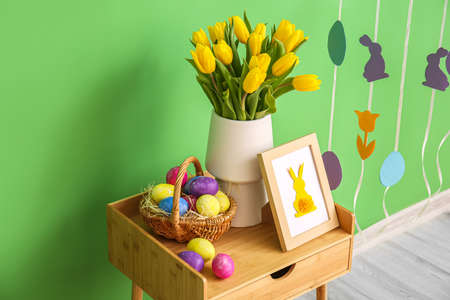 Basket with Easter eggs, photo frame and vase with tulips on table near color wallの写真素材