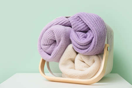 Basket with rolled sweaters on table near color wallの写真素材