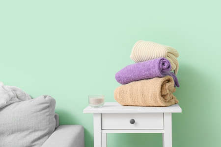 Stack of knitted sweaters and candle on table near color wallの写真素材