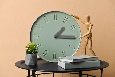 Table with modern clock, books and mannequin near color wall in room
