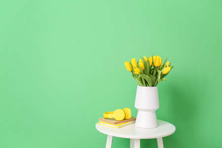 Vase with beautiful tulips, notebooks and headphones on table near color wallの写真素材
