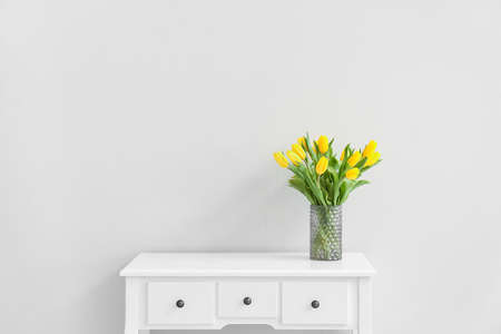 Vase with beautiful tulips on table near light wallの写真素材