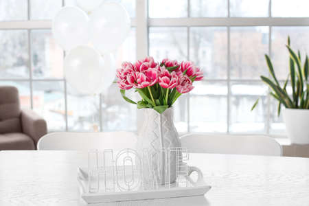 Vase with tulips and word HOME on table in light room