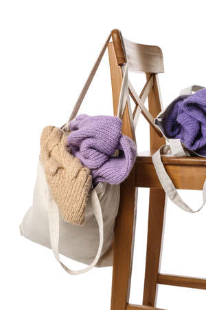Bags with knitted sweaters on wooden chair against white backgroundの写真素材