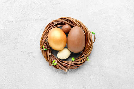 Nest with different chocolate Easter eggs on light background