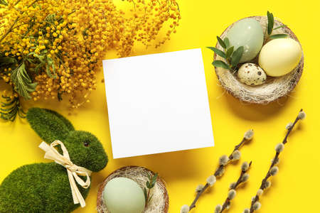 Beautiful Easter composition with blank card, eggs and mimosa branches on yellow backgroundの写真素材