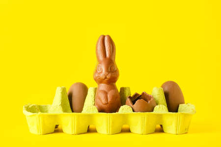 Holder with chocolate Easter bunny and eggs on yellow background
