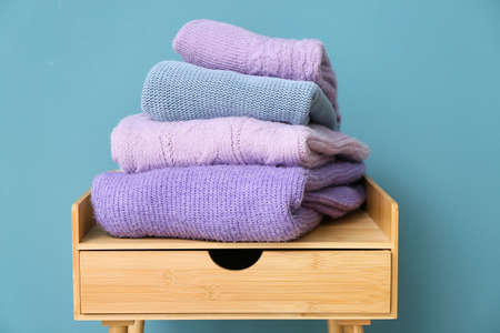 Stack of stylish sweaters on table near color wallの写真素材