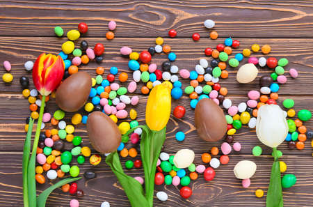 Composition with chocolate Easter eggs, candies and flowers on wooden backgroundの写真素材