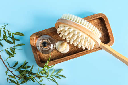 Wooden board with massage brush, bottle of essential oil and plant branch on color backgroundの写真素材