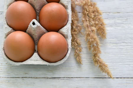 Holder with fresh chicken eggs and spikelets on white wooden background, closeup