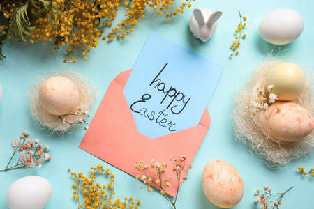 Beautiful Easter composition with greeting card, eggs and mimosa branches on color backgroundの写真素材