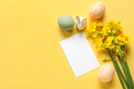 Composition with blank card, beautiful narcissus flowers and Easter eggs on color background