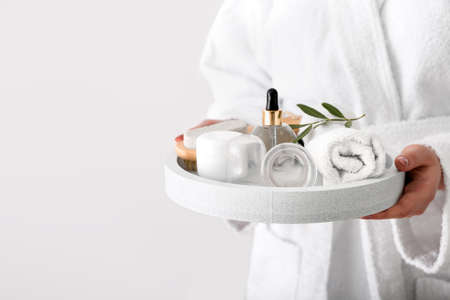 Woman holding tray with bath supplies and vacuum jars for anti-cellulite massage on light backgroundの写真素材