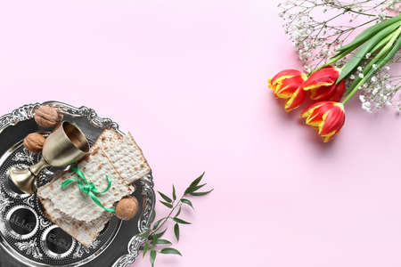 Composition with Passover Seder plate, flatbread matza and flowers on pink background