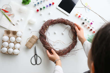 Woman making beautiful Easter wreath on light table