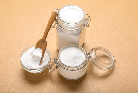 Jars and bowl with baking soda on beige background
