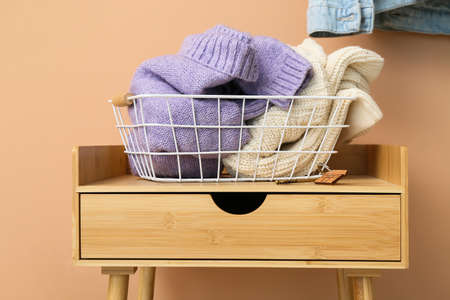 Basket with knitted sweaters on table near beige wallの写真素材
