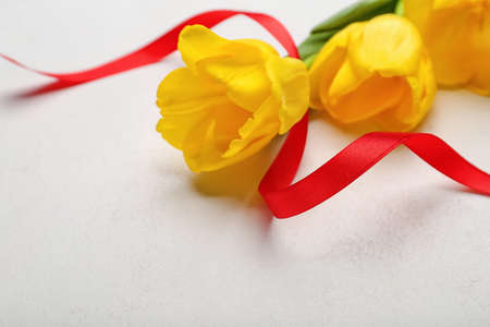 Beautiful tulip flowers and red ribbon for International Women's Day celebration on light background, closeupの写真素材