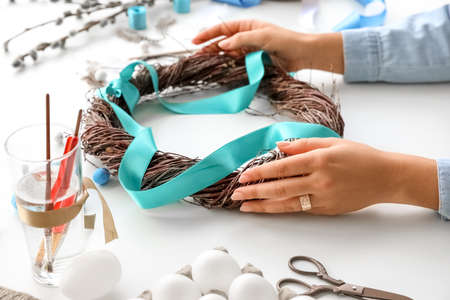 Woman decorating Easter wreath with ribbon on tableの写真素材