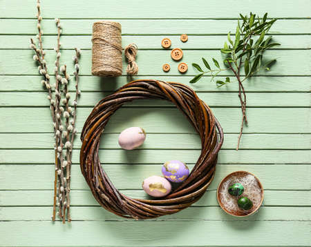 Composition with wreath, Easter eggs, pussy willow branches and rope on green wooden background