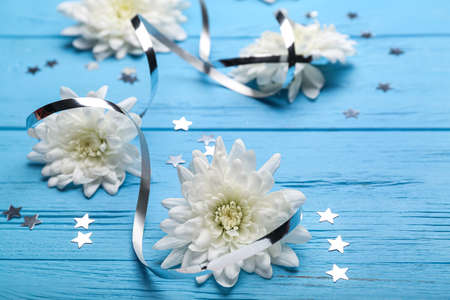 Composition with white chrysanthemum flowers and confetti on color wooden background, closeup....