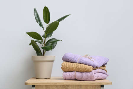 Stack of knitted sweaters and houseplant on table near light wallの写真素材