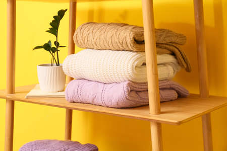 Stack of knitted sweaters and houseplant on shelf near yellow wallの写真素材