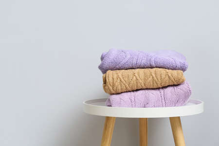 Stack of knitted sweaters on table near light wallの写真素材