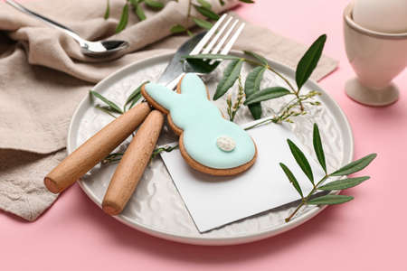 Stylish table setting with Easter cookie on pink background