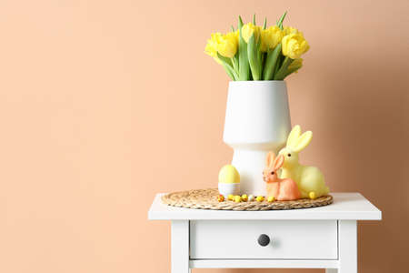 Vase with tulips, Easter eggs and rabbits on table near color wall