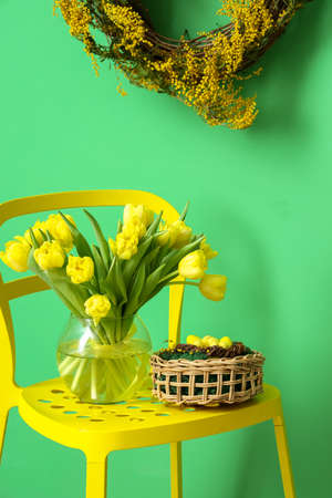Vase with tulips and basket with Easter eggs on chair near color wallの写真素材