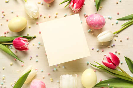Beautiful Easter composition with blank card, painted eggs and flowers on light wooden backgroundの写真素材