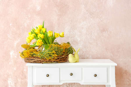 Nest with beautiful flowers and Easter decor on table near color wallの写真素材