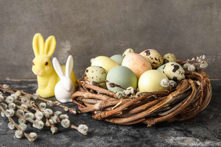 Nest with painted Easter eggs, bunnies and pussy willow branches on dark background