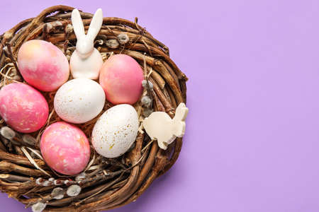 Nest with painted Easter eggs, bunny and pussy willow branches on purple backgroundの写真素材