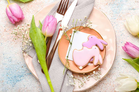 Stylish table setting with Easter cookies on light grunge background