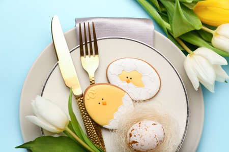 Stylish table setting with Easter cookies on blue background