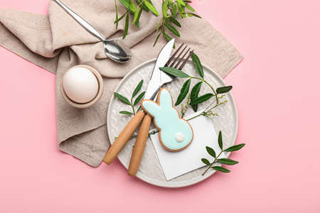 Stylish table setting with Easter cookie on pink background